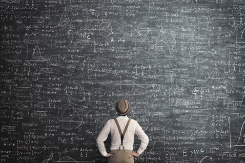 man solving equations on blackboard