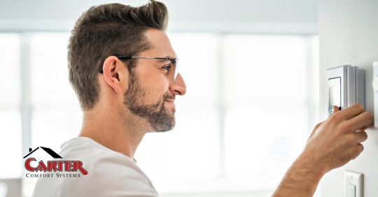 An adult man adjusting a thermostat attached to a wall.