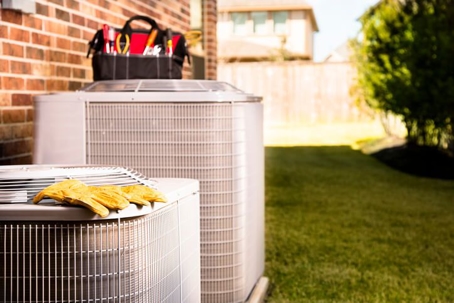 An outdoor AC unit with a technician's toolbox on top and a pair of yellow gloves
