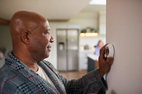An adult man adjusting his thermostat.